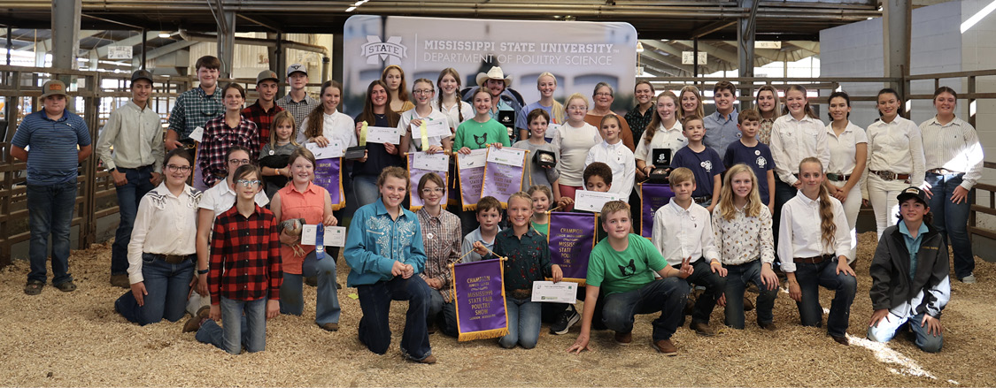 A group 45 people, both adults and children, line up in roughly three rows. The prize winners are holding their award banners and checks. Everyone is full of smiles.