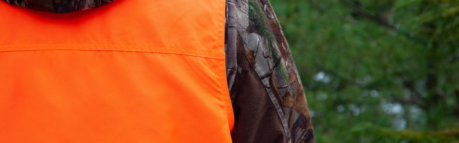 The back of a hunter wearing a camouflage jacket and an orange hunting vest