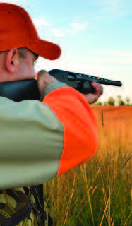 A hunter wearing orange cap and orange on his sleeves, practices safety while aiming a rifle.